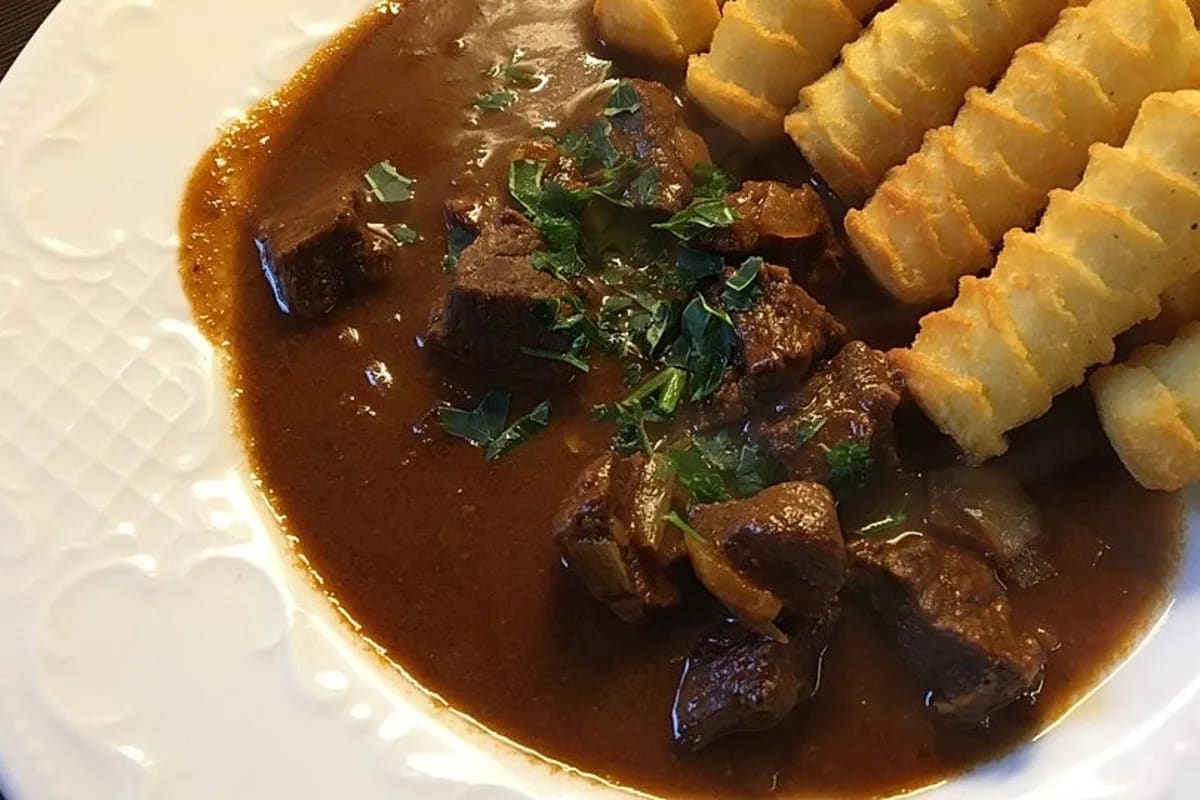 Dampfender Topf mit Gulasch, brauner Schokoladenspiegel und frischer Petersilie