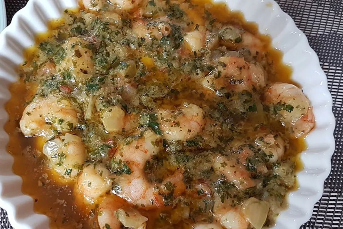 Gebratene Garnelen in goldgelbem Knoblauch‑Chili‑Öl, garniert mit frischer Petersilie auf einer rustikalen Holzplatte