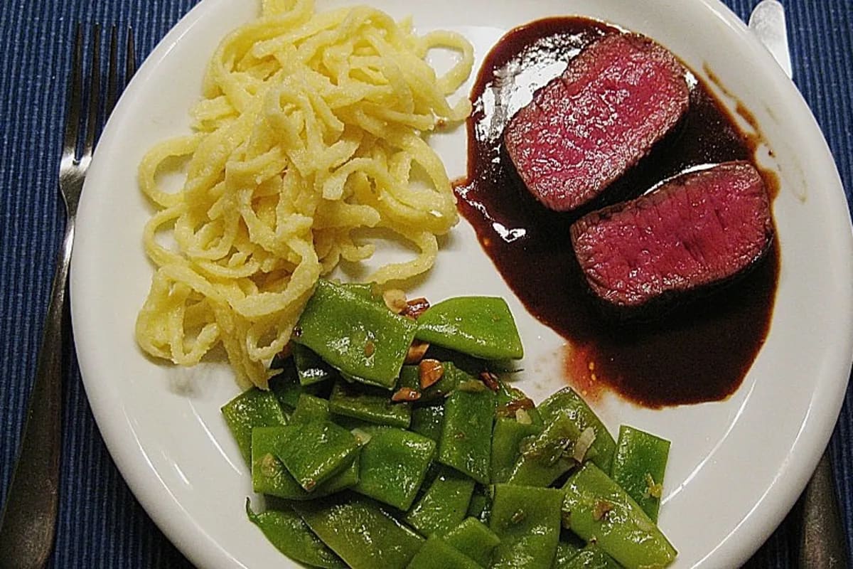 Hirschrückensteak in dunkler Rotwein‑Preiselbeersauce, daneben grüne Bohnen und Spätzle