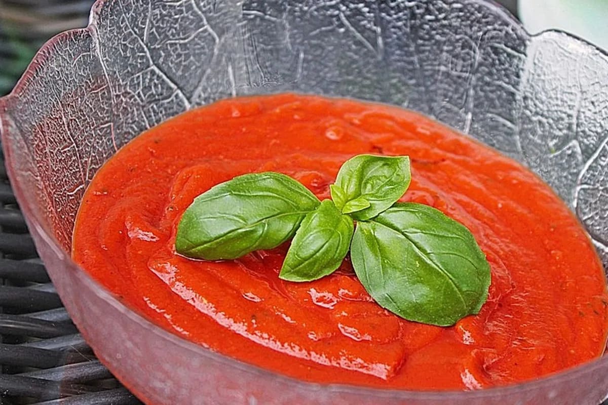 Glas mit frisch zubereiteter roter Pizzasauce, daneben ein Holzlöffel und ein Bündel Basilikum