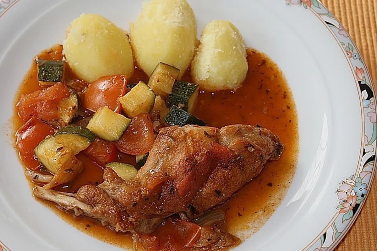 Goldbraun angebratene Kaninchenteile in einem rustikalen Bräter mit Tomaten und Zucchini