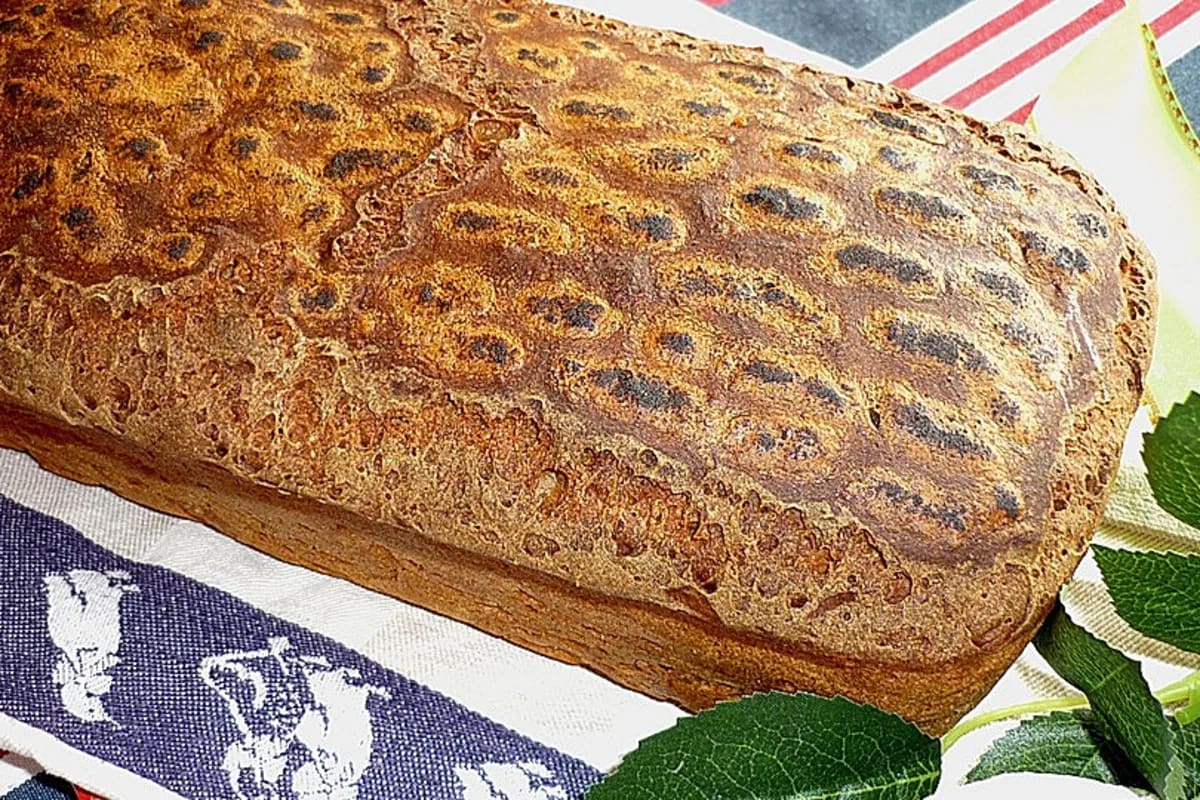 Frisches Gersterbrot mit dunklen, leicht gebrannten Flecken auf der Kruste, aus einer Holzschale gestürzt