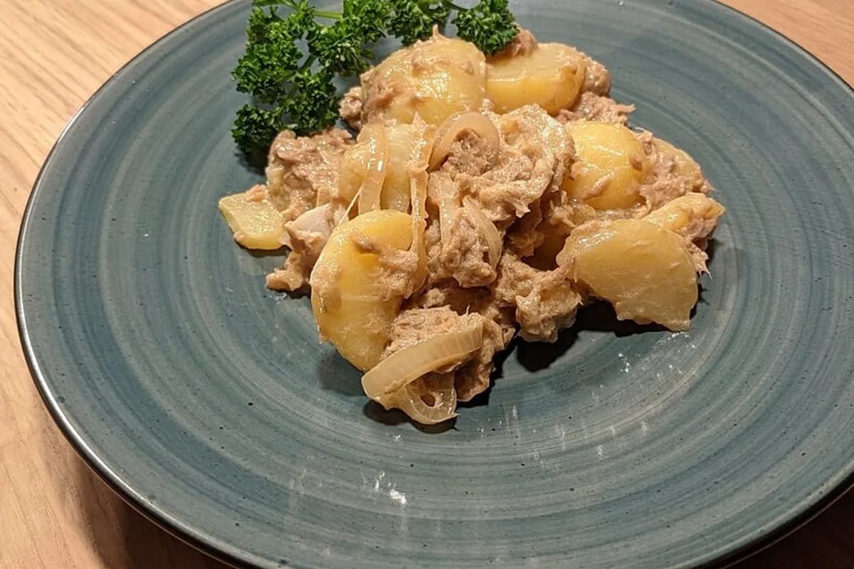 Kartoffelsalat mit Thunfisch, garniert mit Sesam und frischem Pfeffer auf einem rustikalen Holztisch