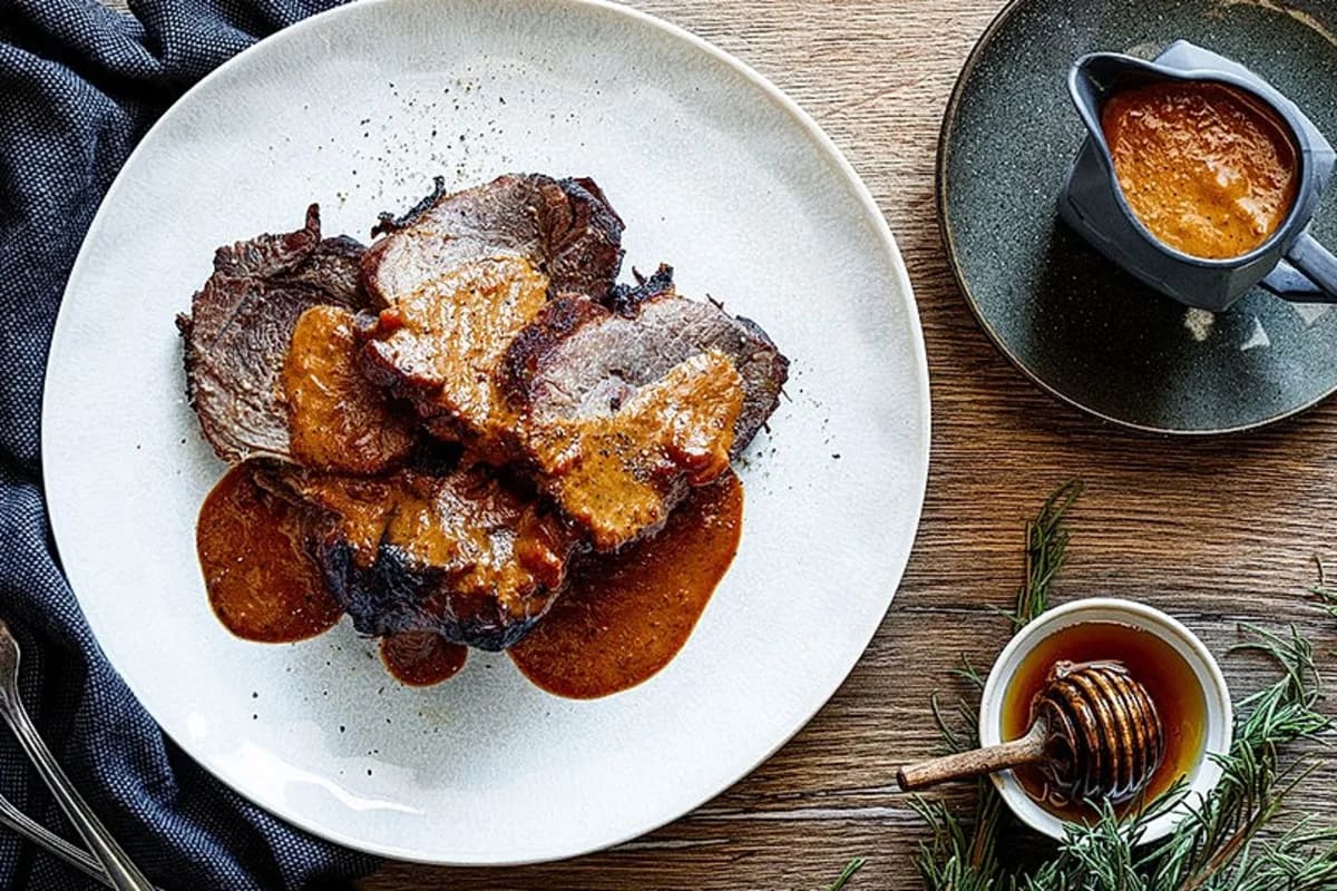 Goldbraun geschmorte Wildschweinkeule mit glänzender Sauce, umgeben von Karotten und Zwiebeln