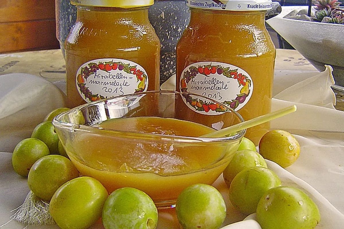 Glas mit roter Mirabellenmarmelade, daneben frische Mirabellen und ein Löffel
