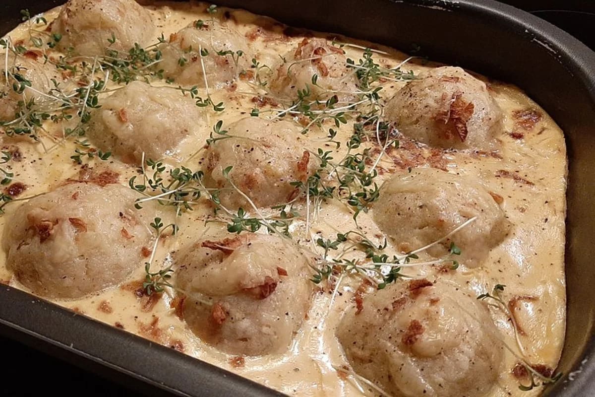 Knödel-Sauerkraut-Auflauf in einer Auflaufform, oben knusprig gebackener Käse, servierfertig auf rustikalem Holztisch