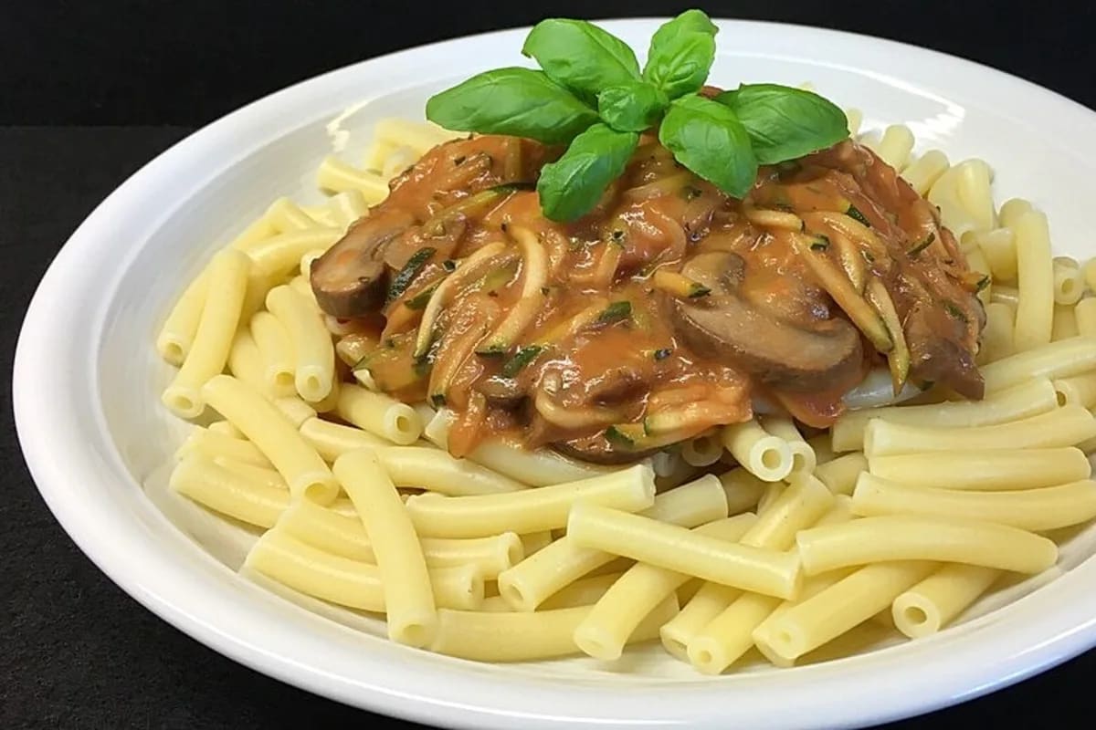 Pasta mit Zucchini, Champignons und Tomatensauce, angerichtet in einer Schüssel mit frischem Basilikum