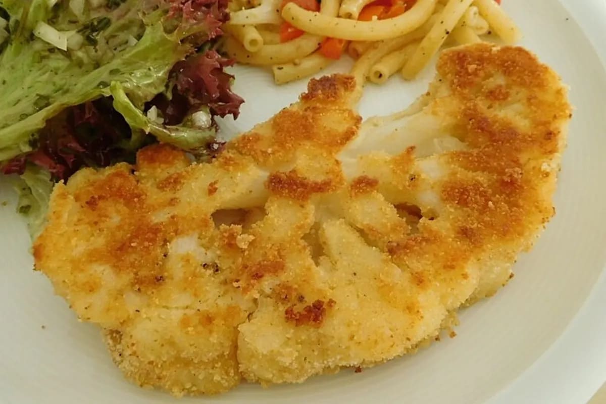 Goldbraun gebratene Blumenkohlschnitzel mit knuspriger Panade auf Holzbrett, garniert mit Petersilie