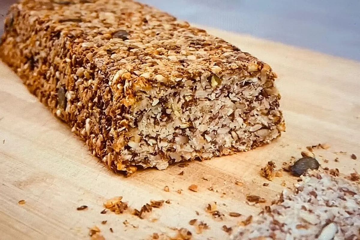 Goldbraunes Saatenbrot mit knuspriger Kruste, aus der Backform genommen, auf einem Holzbrett serviert.