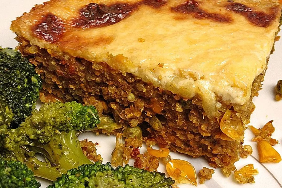 Vegan überbackener Getreideauflauf mit goldbraunem Hefeschmelz, umgeben von frischem Gemüse