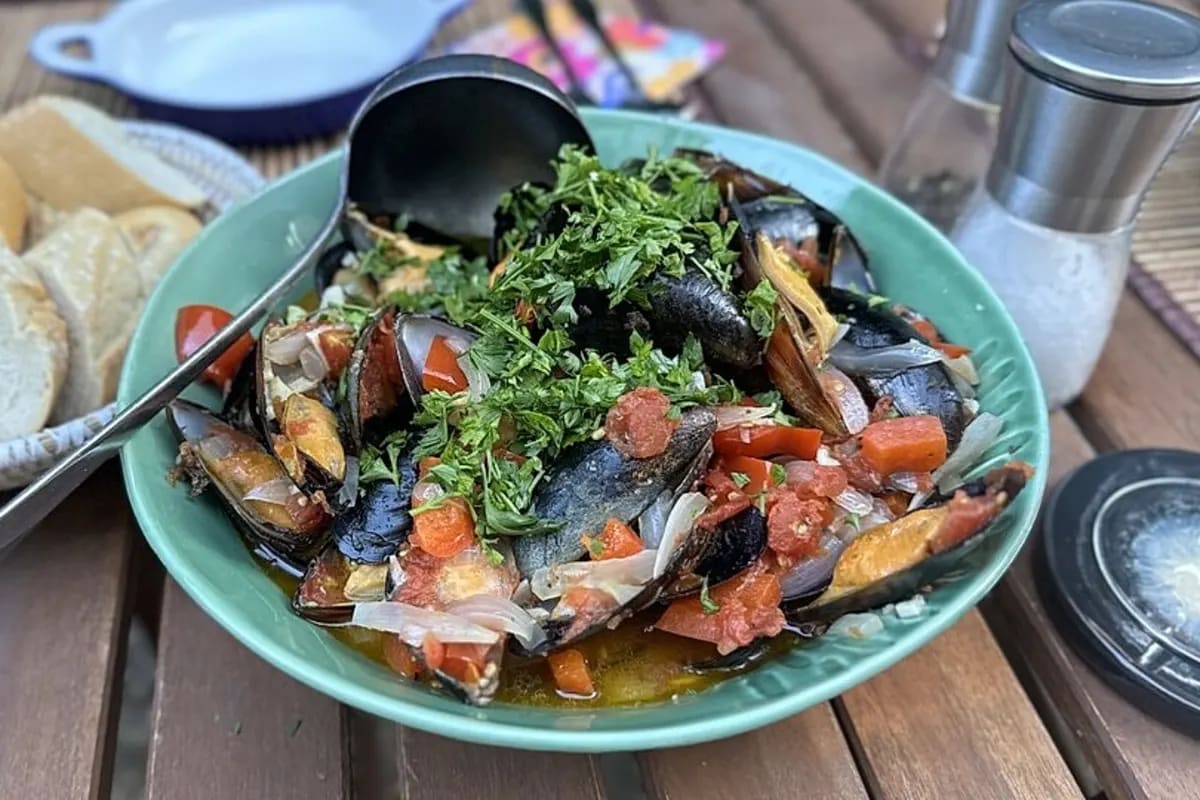 Dampfende Muscheln in roter Tomatensauce, garniert mit grüner Petersilie, daneben knuspriges Baguette.