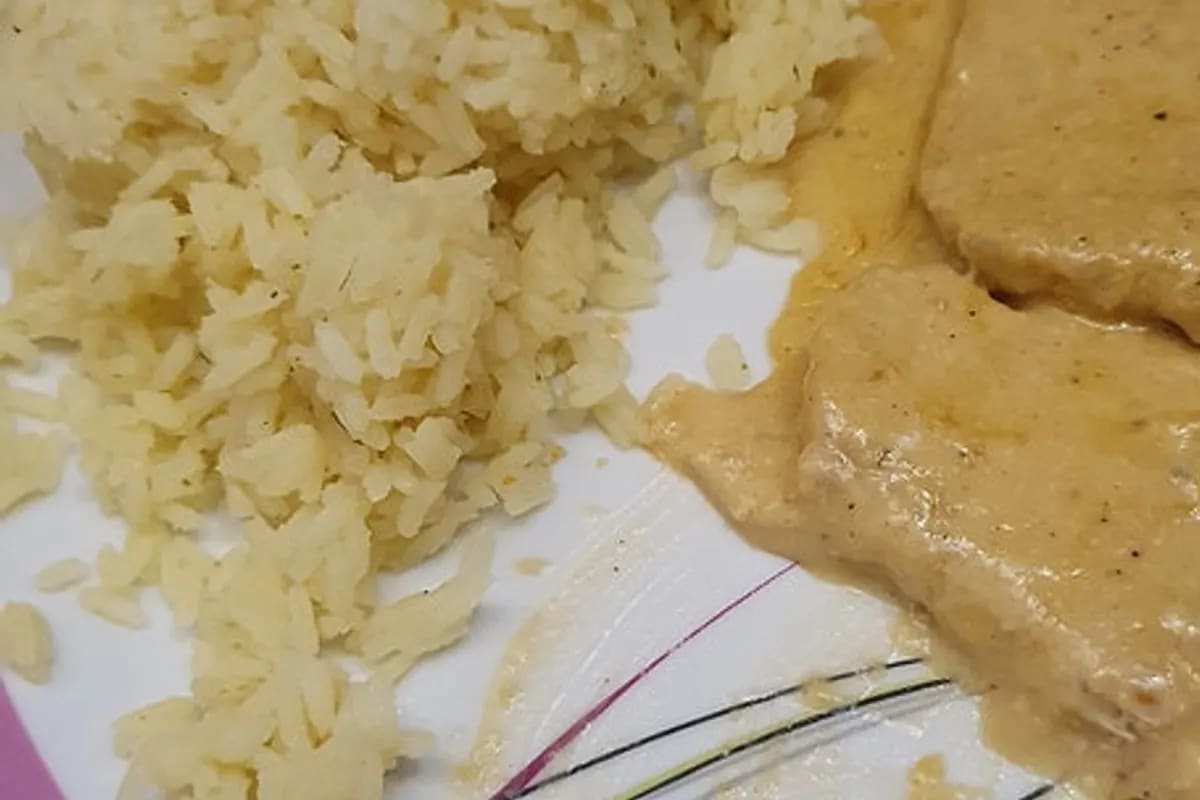 Gebratene Schweine-Minutensteaks mit geschmolzenem Emmentaler, cremiger Sahnesauce und fluffigem Reis, garniert mit grünen Erbsen