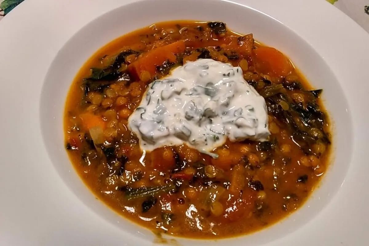 Cremiges rotes Linsen‑Süßkartoffel‑Curry in einer Schüssel, garniert mit Joghurt‑Dip und frischer Petersilie