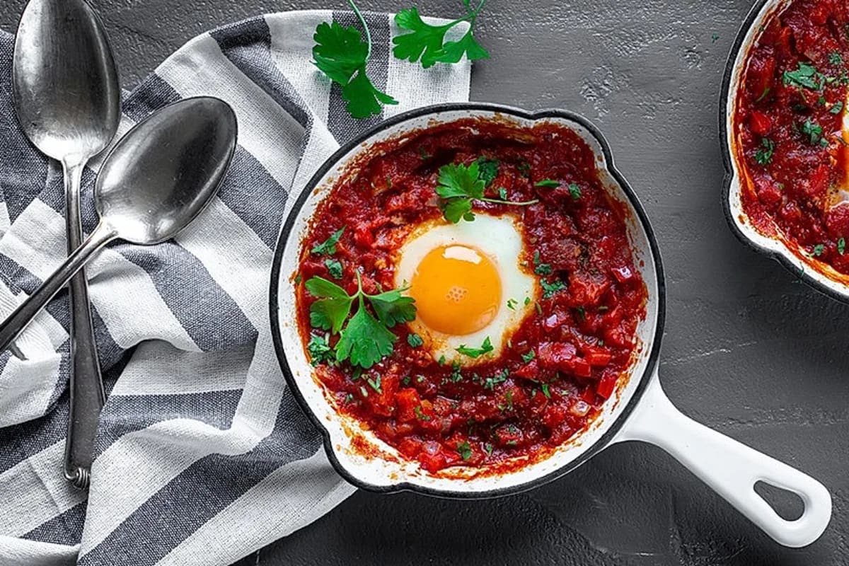 Pfanne mit roter Shakshuka, Eier leicht flüssig, frische Kräuter darüber