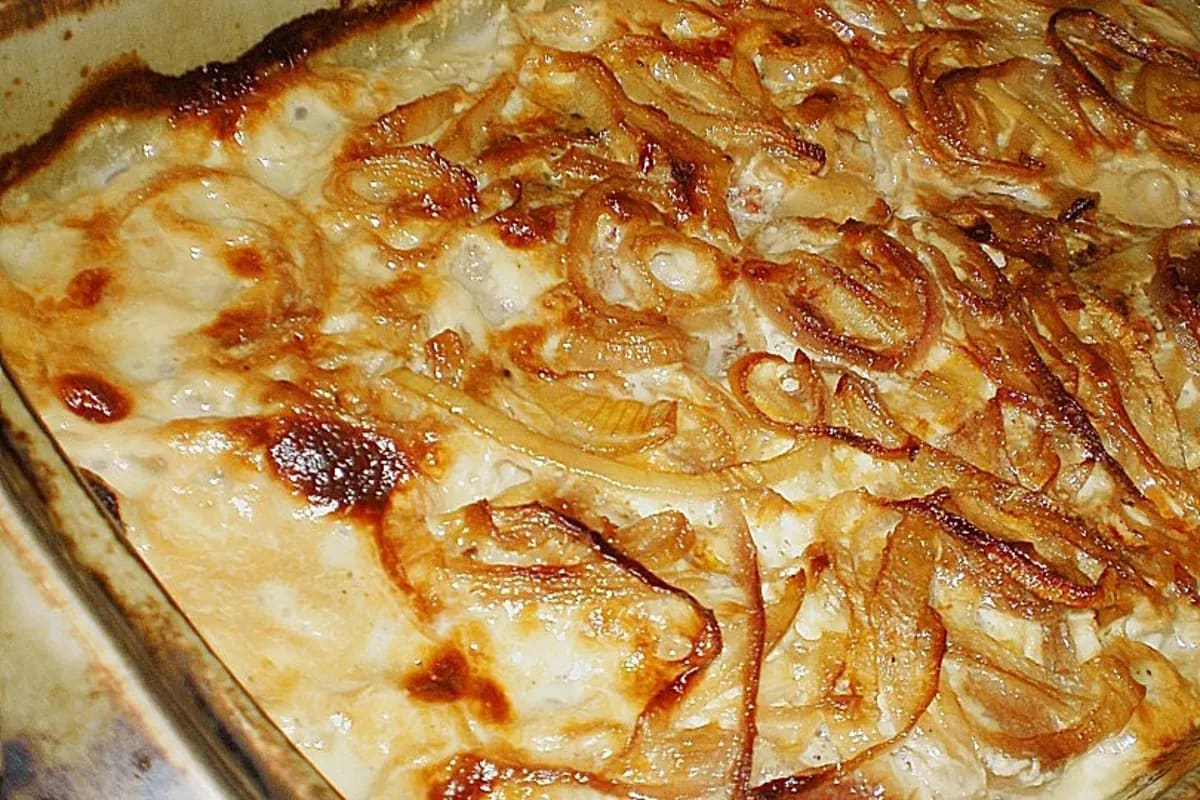 Goldbraun gebratenes Schnitzel mit Zwiebelringen in cremiger Sahnesoße, daneben ein Sesamring