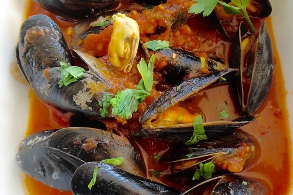 Schale mit dampfender italienischer Miesmuschelsuppe, rote Tomaten, frische Petersilie und knusprigem Brot