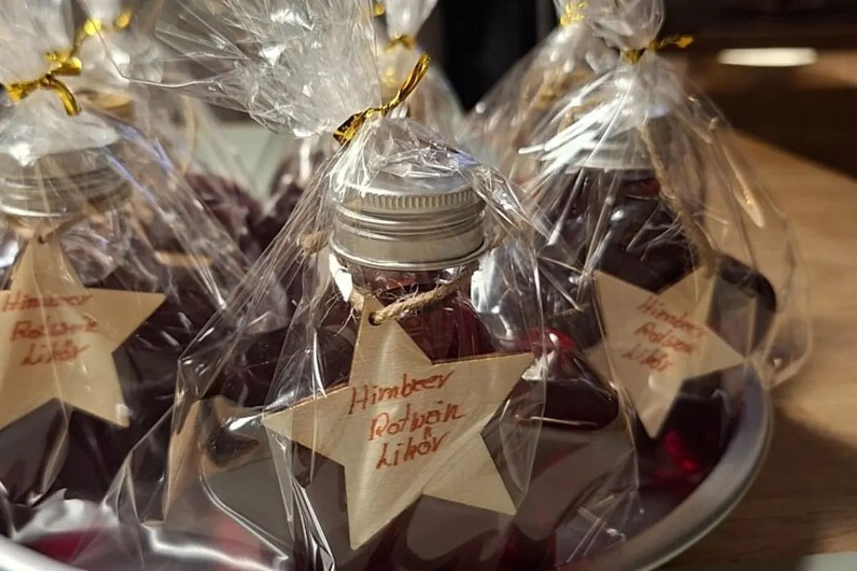Gläser mit rubinrotem Himbeer‑Rotwein‑Likör neben frischen Himbeeren und einer Flasche Korn