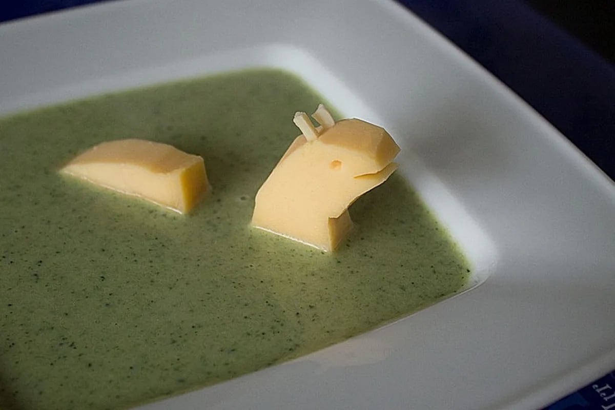 Dampferhitzende Schüssel mit grüner Brokkoli-Creme-Suppe, garniert mit Frischkäse-Streuseln und knusprigen Croûtons