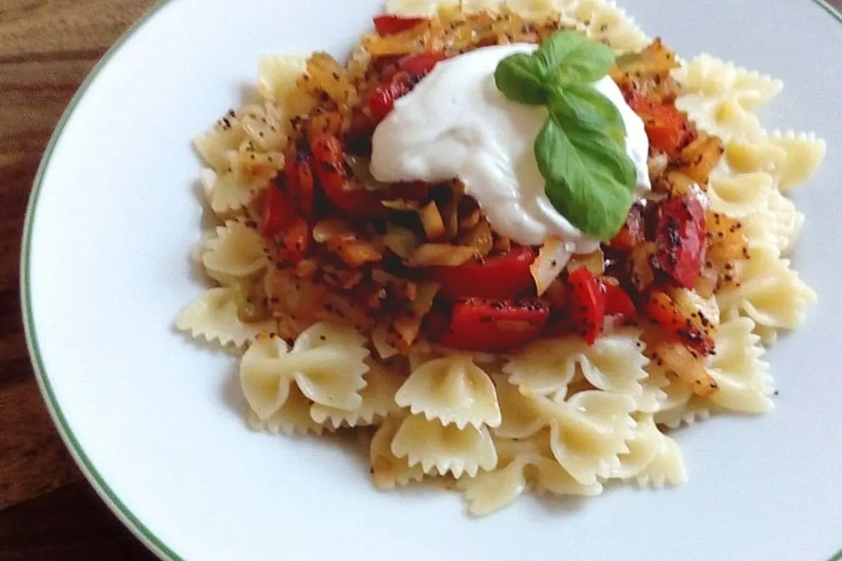 Farfalle mit blanchierter Paprika, Weißkohl, Mohn und cremiger Quark‑Sauce angerichtet auf einem rustikalen Holzbrett