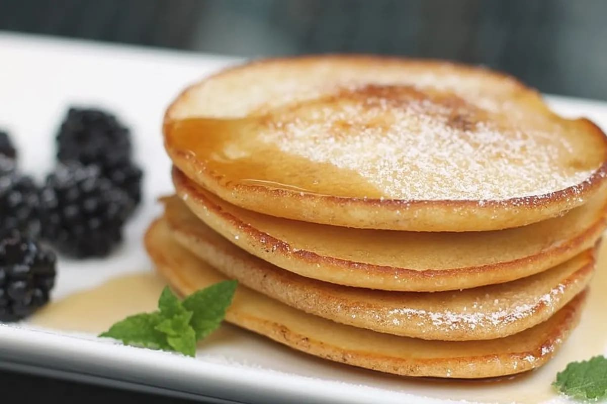 Goldgelbe Mini Pancakes auf einem Teller, garniert mit Ahornsirup und frischen Beeren