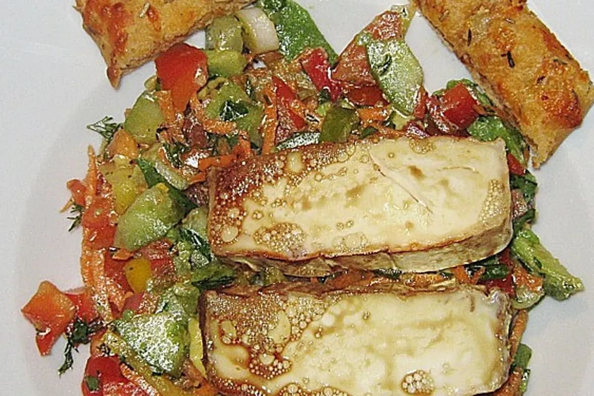 Bunter Salat mit goldbraun gebackenem Ziegenkäse, Limetten‑Dressing, Avocado und frischen Kräutern auf weißem Teller