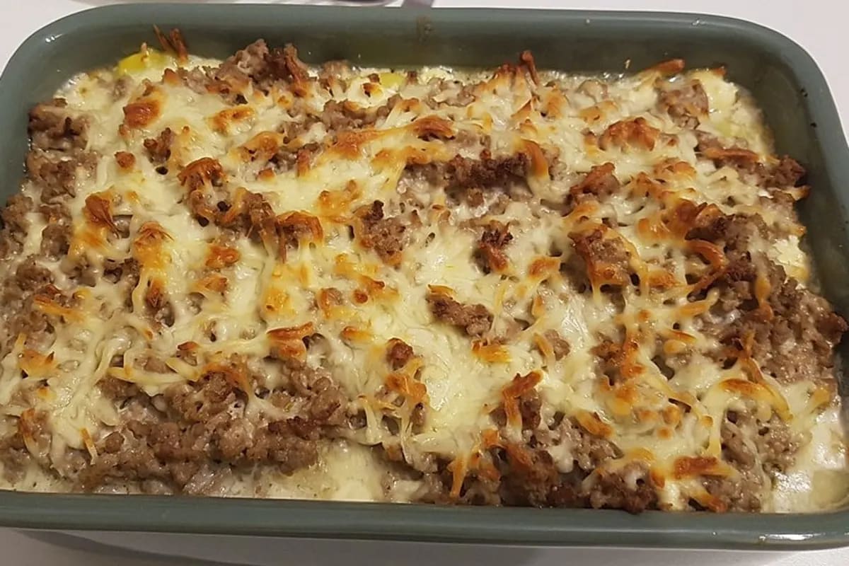 Goldbrauner Kartoffel-Hack-Feta-Auflauf aus einer Auflaufform, mit geschmolzenem Käse und frischen Kräutern bestreut