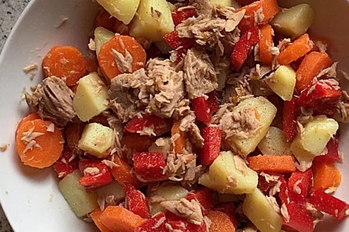 Bunter spanischer Kartoffelsalat mit Knoblauchscheiben, Paprika und Thunfisch auf einem rustikalen Holzbrett