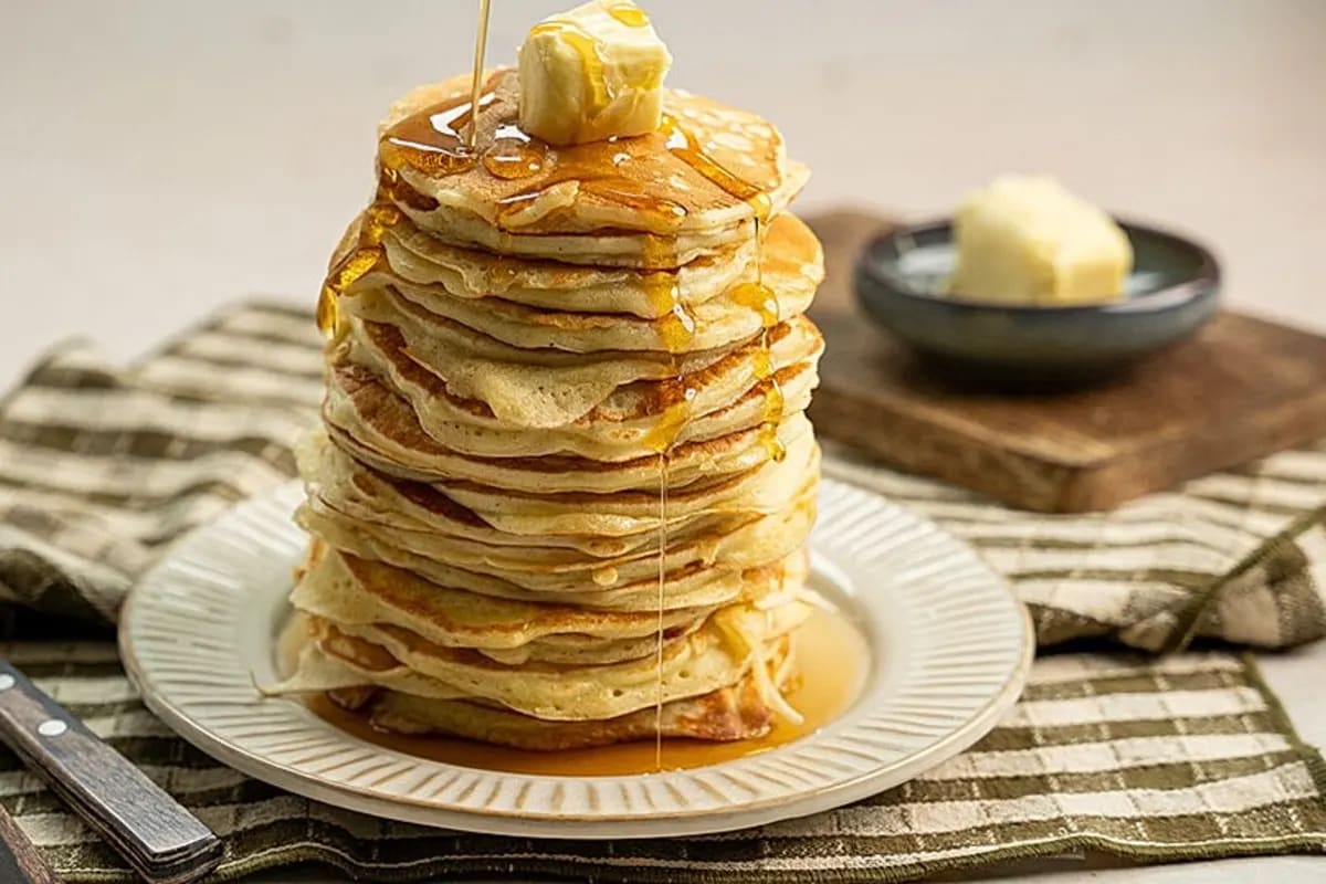 Goldbraune Pfannkuchen gestapelt, übergossen mit glänzender Blaubeersauce, bestäubt mit Puderzucker