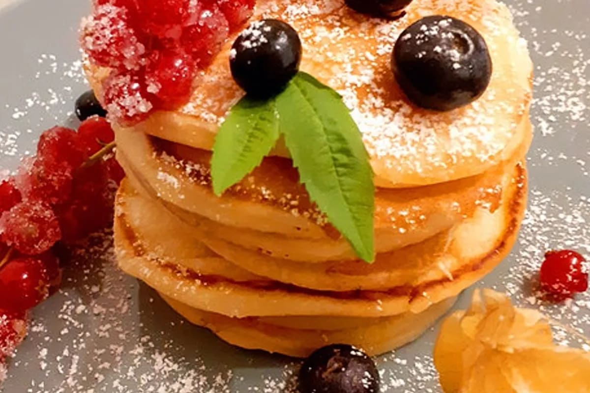 Goldbraun gebratene amerikanische Pfannkuchen, gestapelt, mit Ahornsirup übergossen und einem Stück Butter daneben