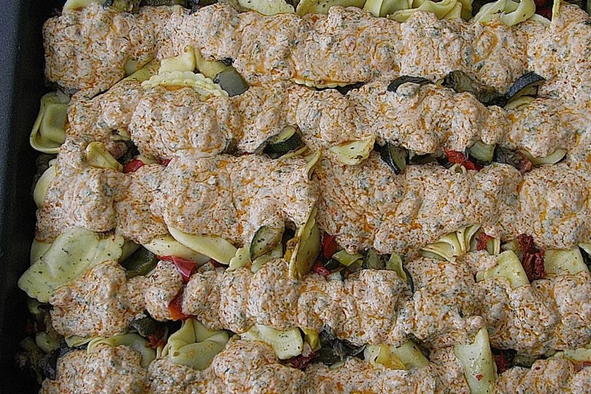 Bunter Ravioli‑Salat mit grünem Pesto‑Dressing, gebratenen Auberginen, Zucchini und Paprika auf rustikalem Holzbrett