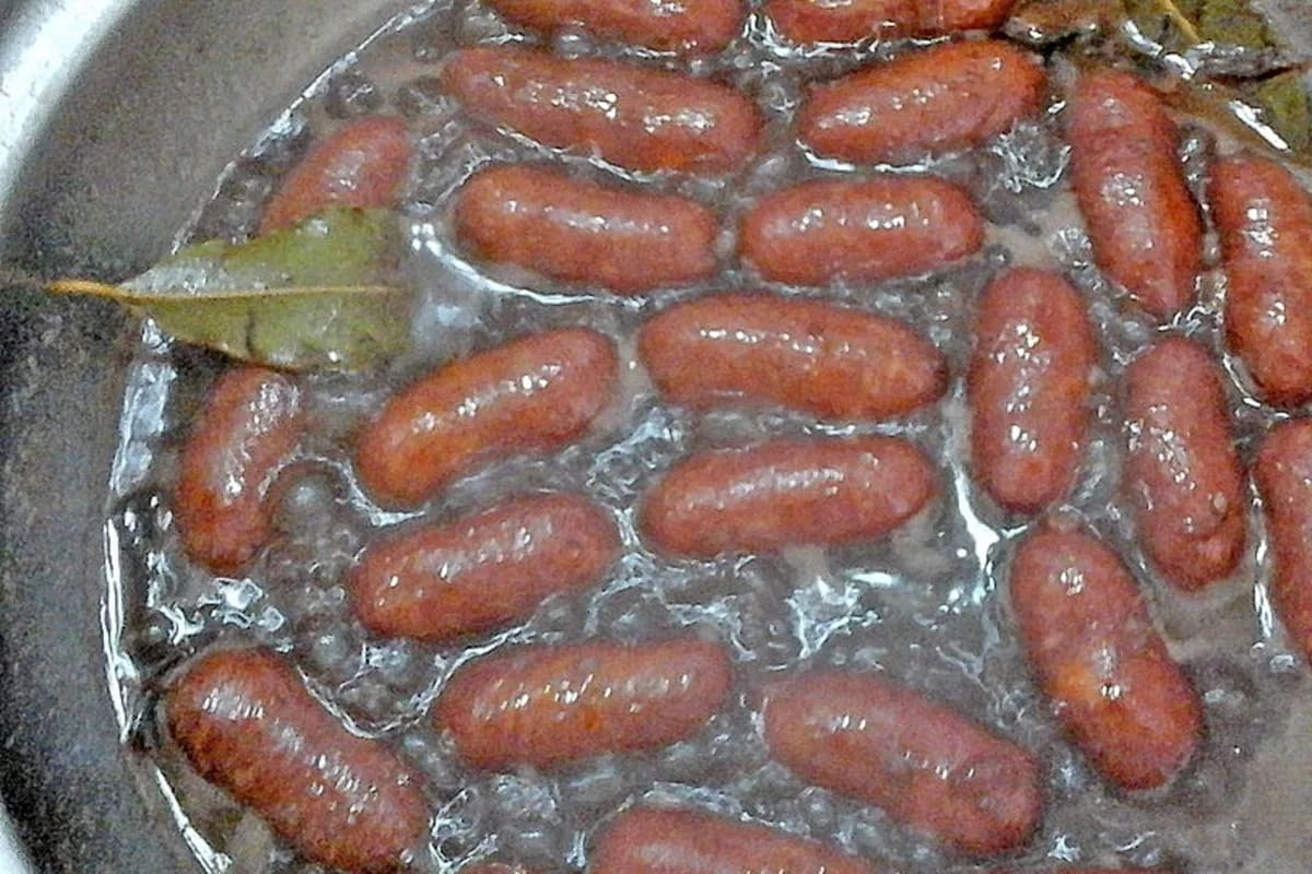 Scheibenweise geschnittene rote Zwiebeln und Bratwürste in dunkler Rotweinsauce auf einem rustikalen Holzbrett