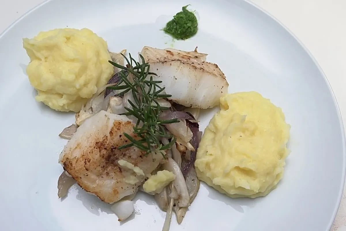 Gebratene Kabeljau Loins neben cremigem Kartoffelstampf und leuchtendem Fenchelpesto auf einem weißen Teller