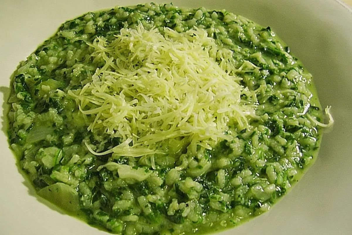 Cremiges Risotto à la Milanese mit leuchtendem Safran, grünem Spinat und goldenen Champignons auf einem weißen Teller