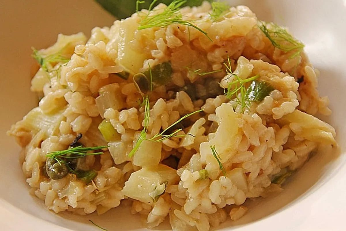 Cremiges Risotto mit leuchtendem Fenchelgrün, Zitronenzesten und Kapern auf weißem Teller
