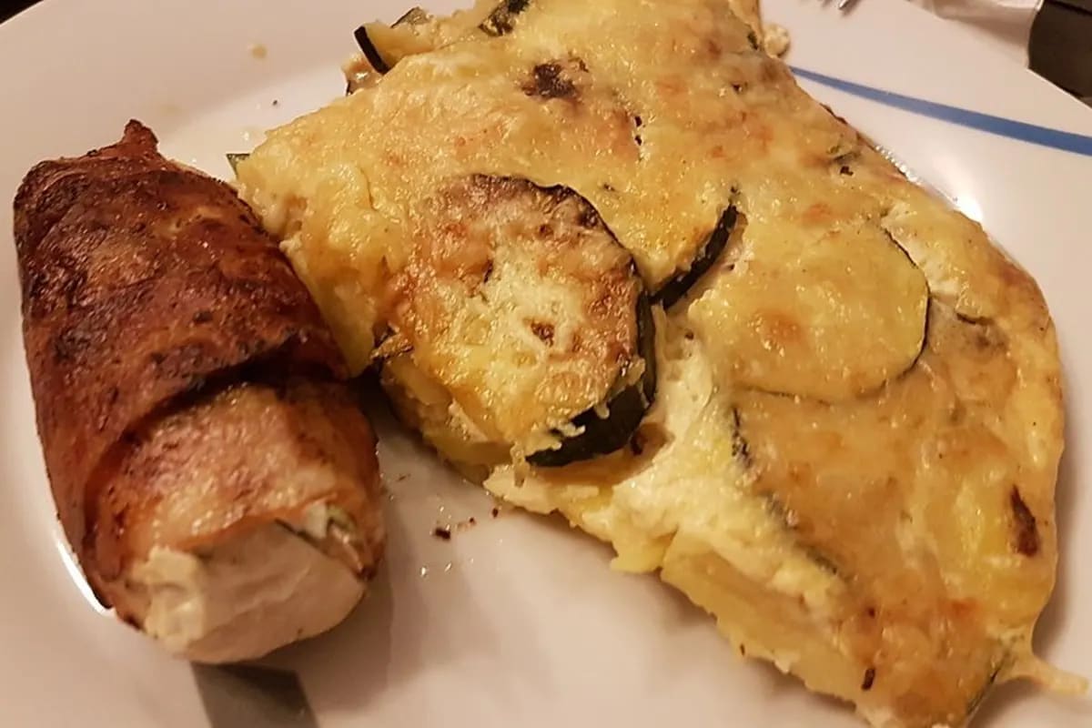 Goldbraune Tortilla mit Zucchini‑ und Kartoffelscheiben, bedeckt mit geschmolzenem Käse und knusprigem Bacon
