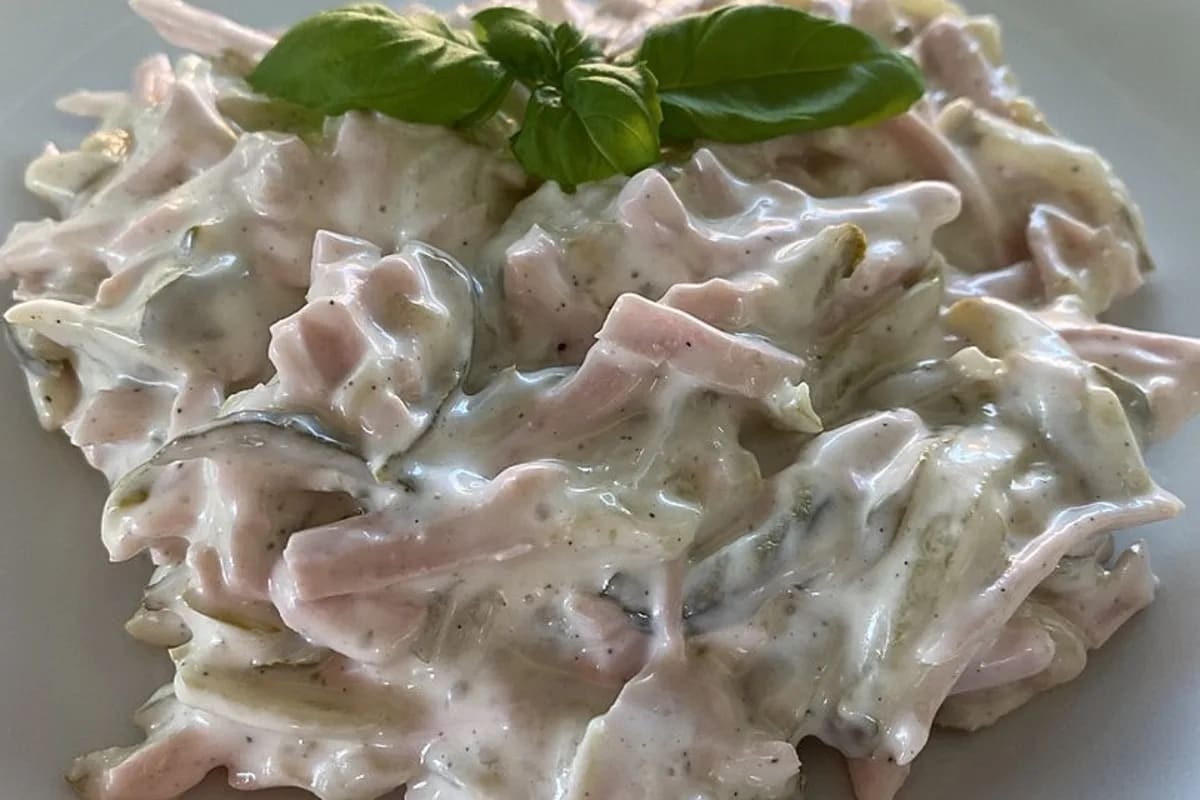 Cremiger Fleischsalat mit goldbraunen Schinkenwurststreifen und frischen Gurkenwürfeln auf einem hellen Teller