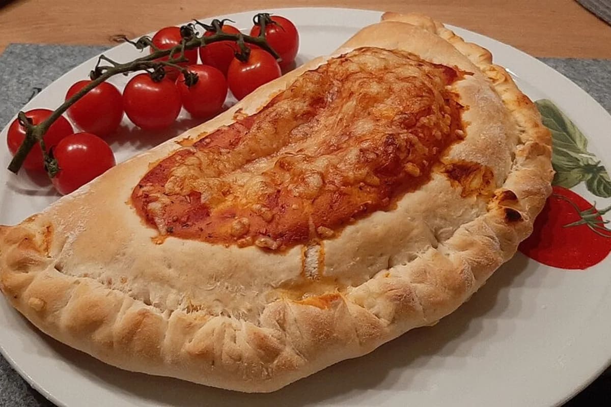 Goldbraune Calzone halbiert, geschmolzener Käse zieht sich heraus, rote Tomatenstücke und knusprige Ränder sichtbar