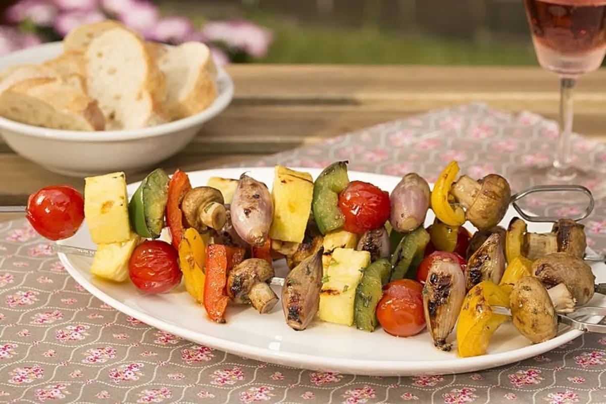 Bunte Gemüsespieße mit gegrillten Pilzen, Paprika, Tomaten und Zwiebeln, angerichtet auf einer Holzplatte