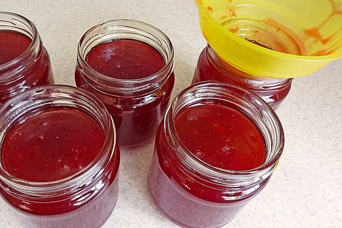 Glas mit tiefroter Mirabellenmarmelade, Zimtstange daneben, rustikaler Holztisch