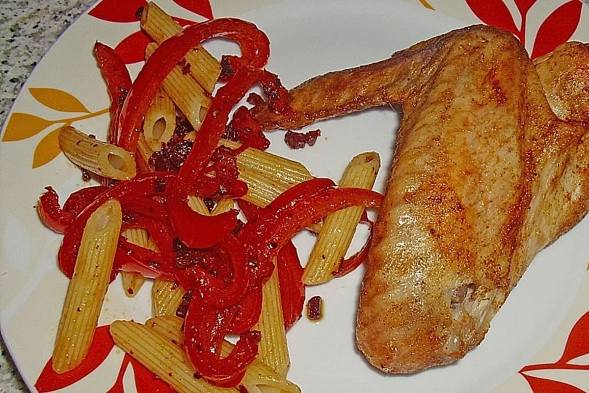 Knusprige Putenflügel auf einem Teller neben goldbraunen Hubertus‑Spätzle mit Paprika, Chili und Speckstückchen