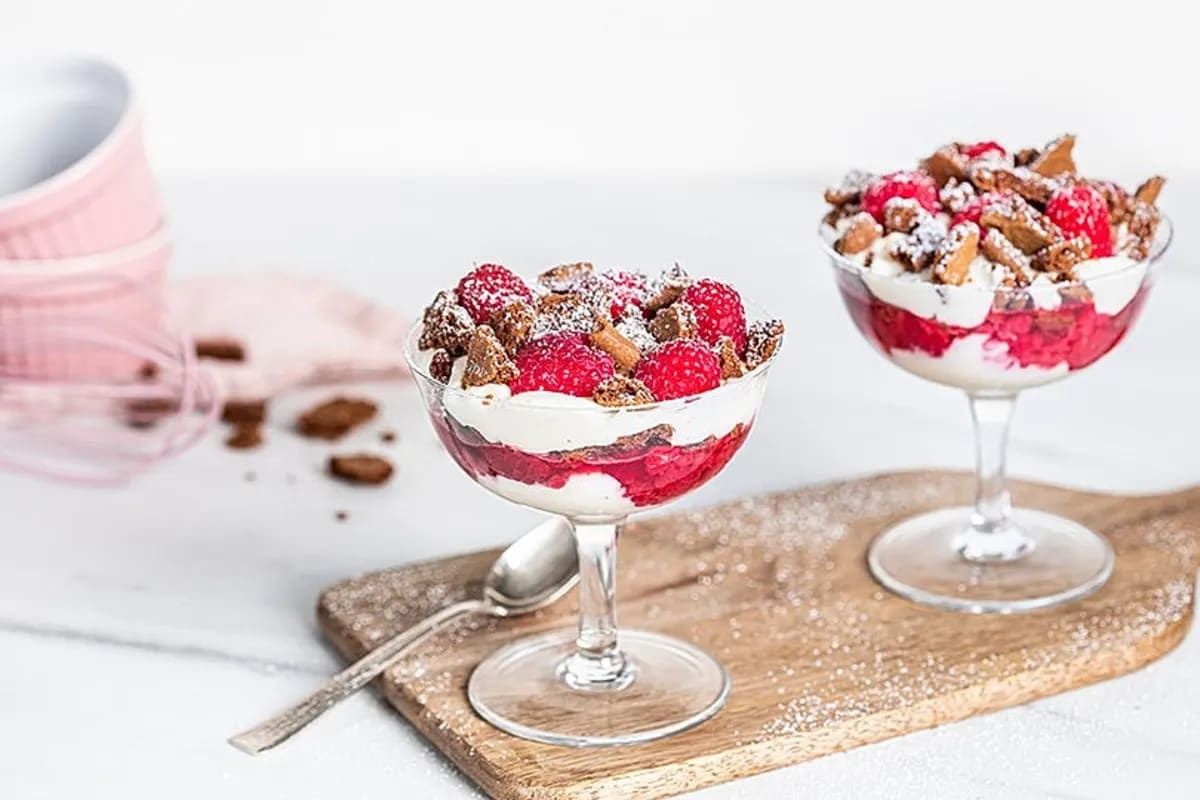 Schichtdessert aus cremiger Himbeer‑Mascarpone‑Mischung, bedeckt mit zerbröseltem Spekulatius, in einer hohen Glaskaraffe serviert