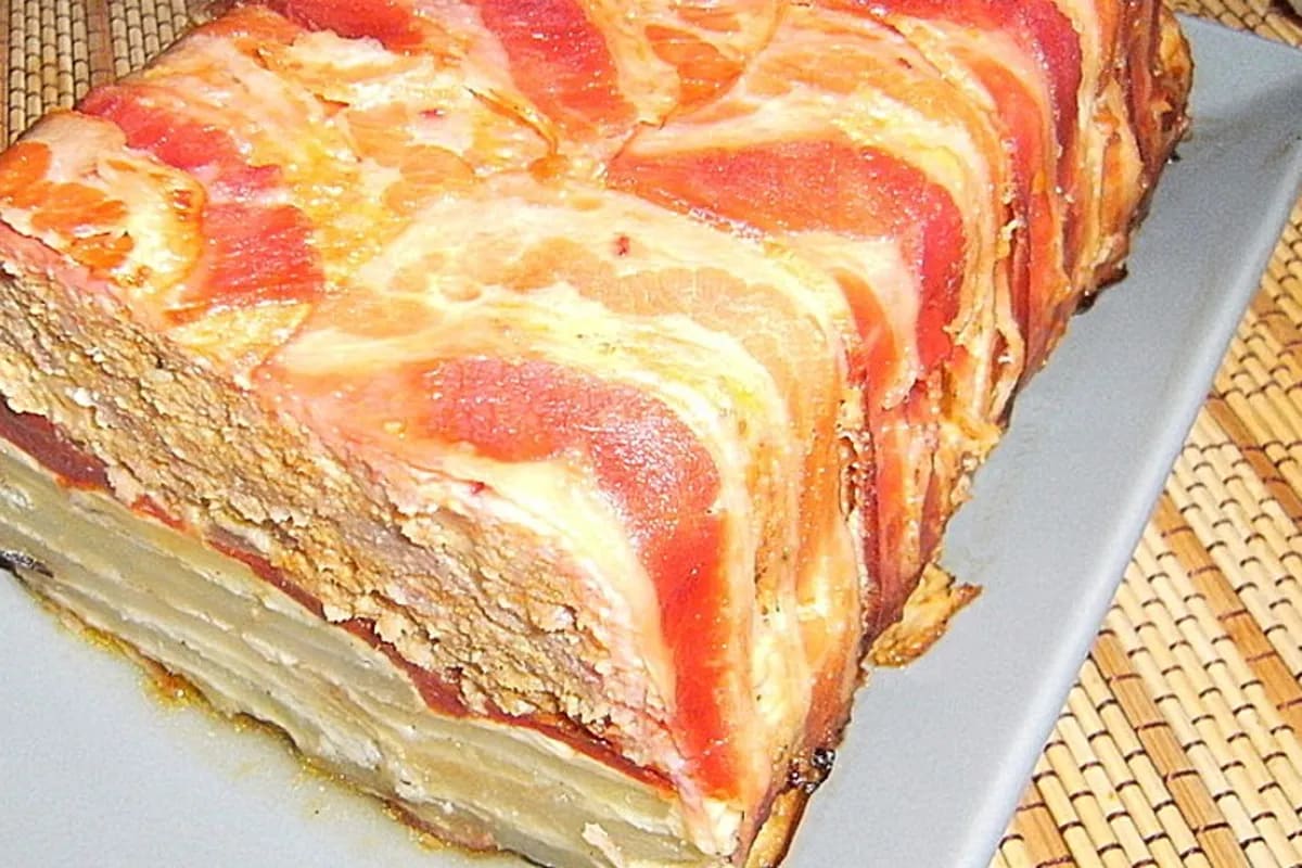 Goldbraun gebackener Pastel de carne mit knusprigem Bacon, schmelzendem Käse und Kartoffelscheiben in einer Kastenform