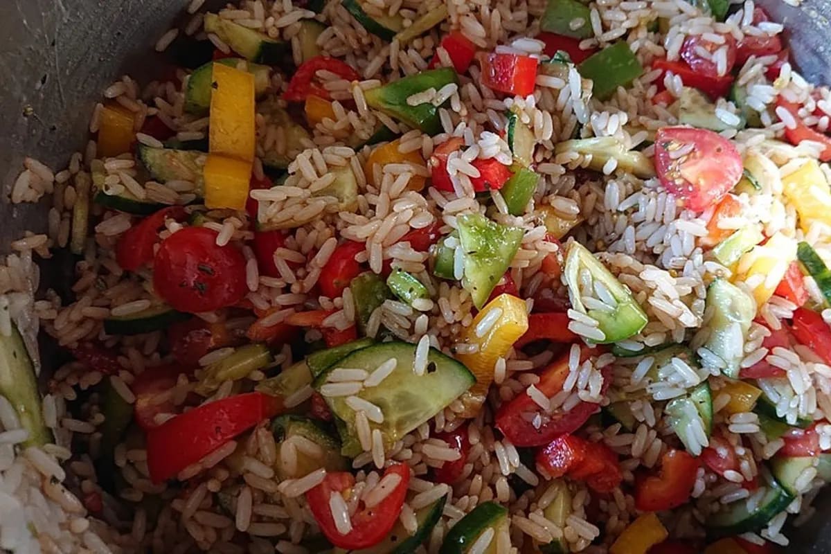 Bunter sommerlicher Reissalat mit roten Paprikawürfeln, grüner Gurke, halbierten Cherrytomaten und frischem Basilikum, angerichtet in einer Glasbowle
