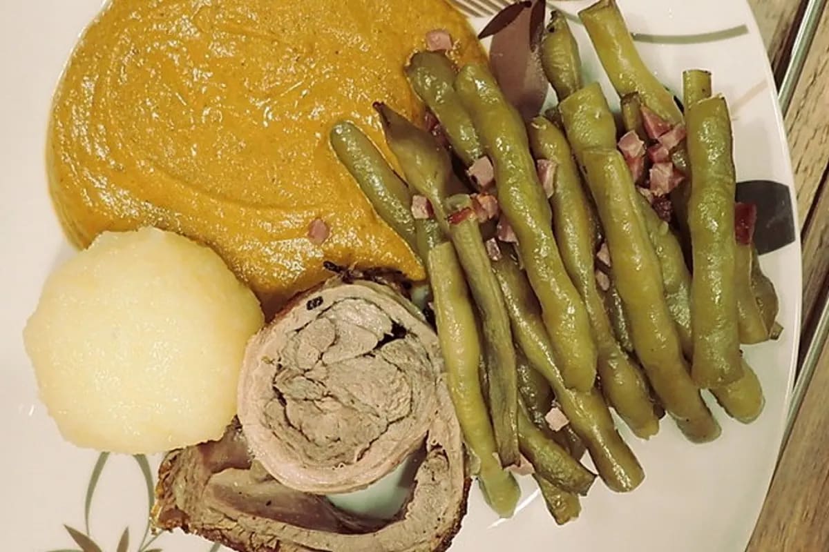 Lammrollbraten mit grünen Bohnen und leuchtend grüner Thüringer Petersiliensoße auf einem rustikalen Holzbrett