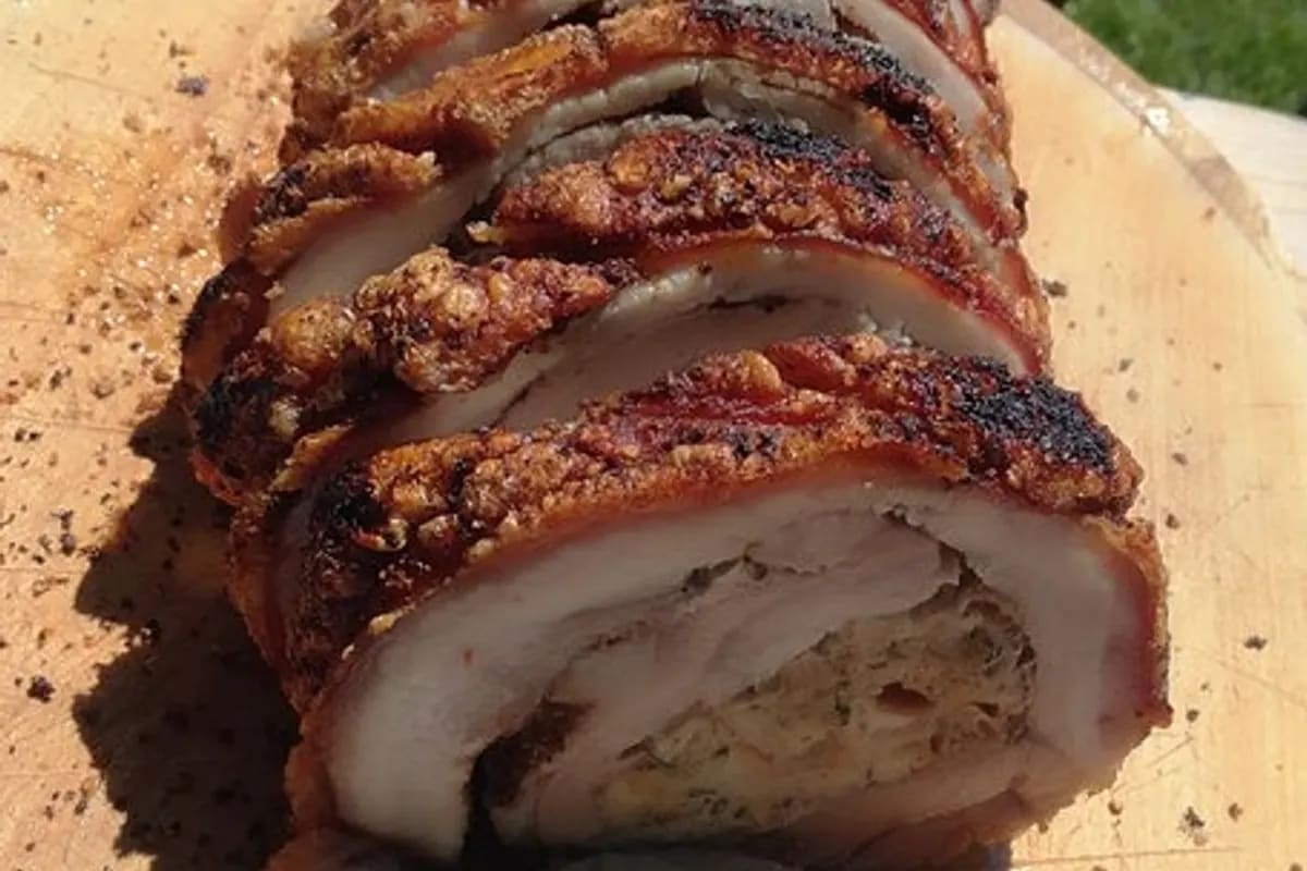 Knusprig gebratener Schweinebauch mit goldener Brezelfüllung auf Holzbrett, Scheiben daneben