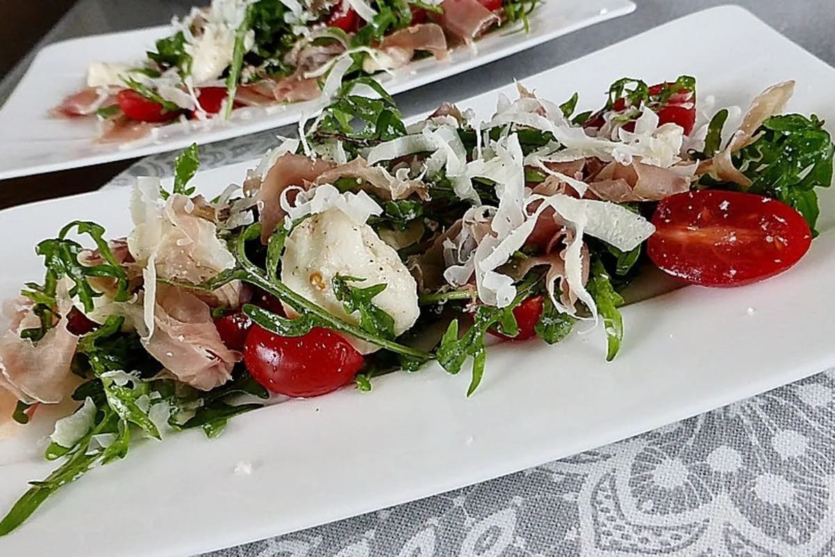 Bunter Rucola Salat mit Kirschtomaten, Mini-Mozzarella und Parmesanspänen auf weißem Teller