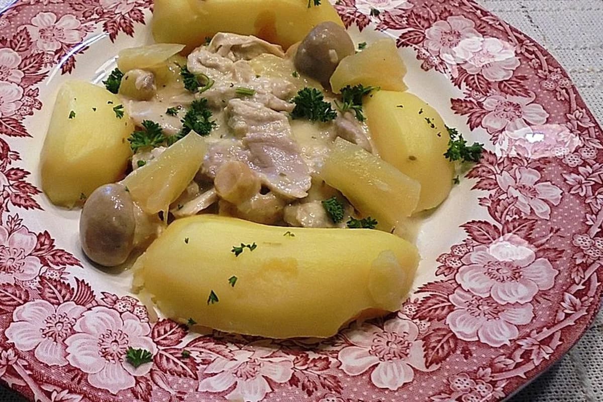 Hähnchenschenkel in cremiger Frikassee mit Karotten, Erbsen und Champignons auf weißem Teller
