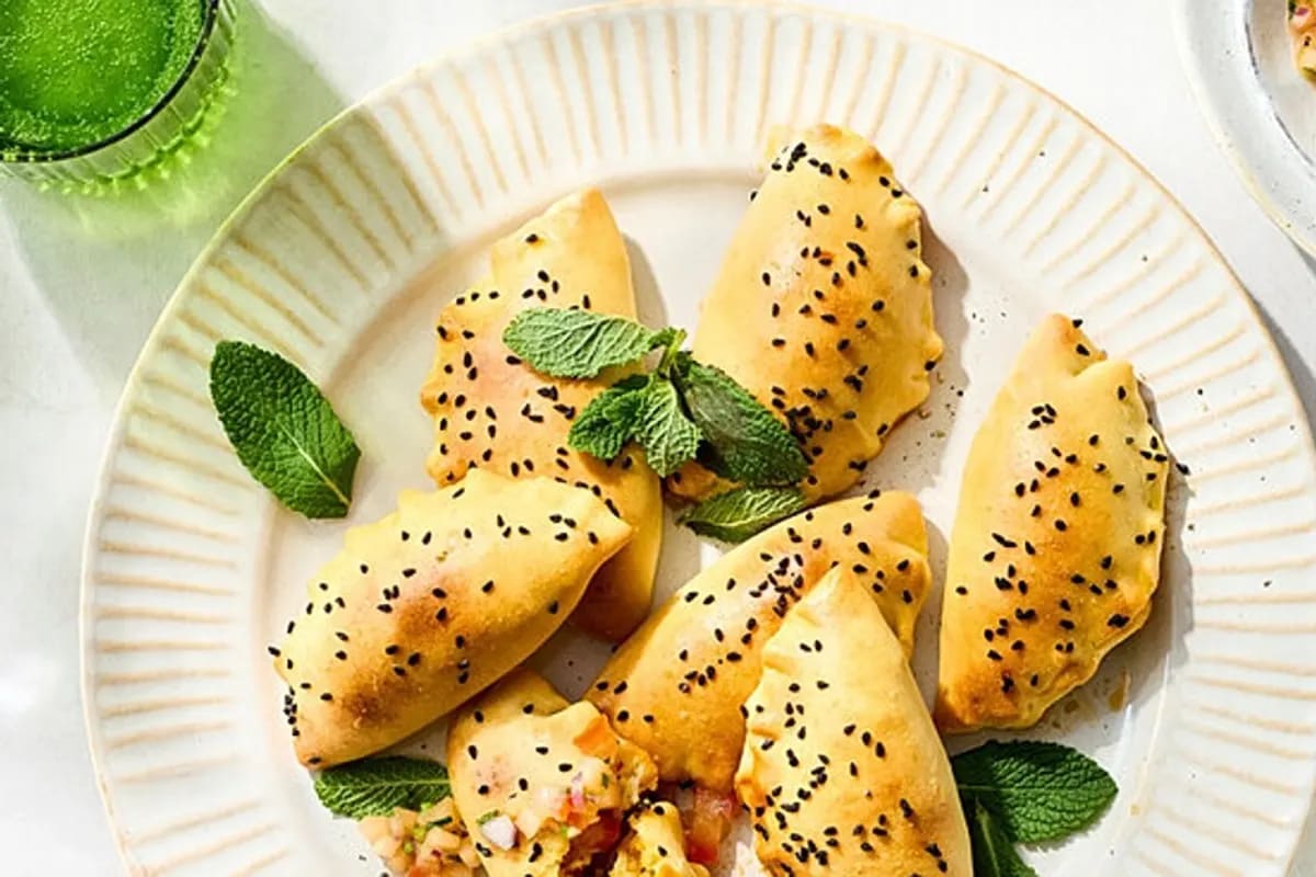 Goldbraun gebackene vegetarische Empanadas auf einem Holzbrett, daneben eine frische, bunte Melonen‑Salsa