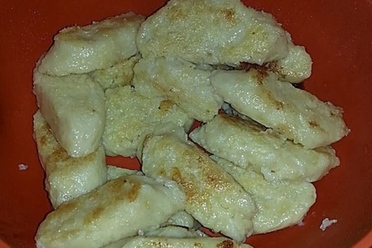 Goldbraune Kartoffelknödel neben rustikalem Sauerkraut, knusprigem Speck und geschmolzener Butter auf einem rustikalen Teller