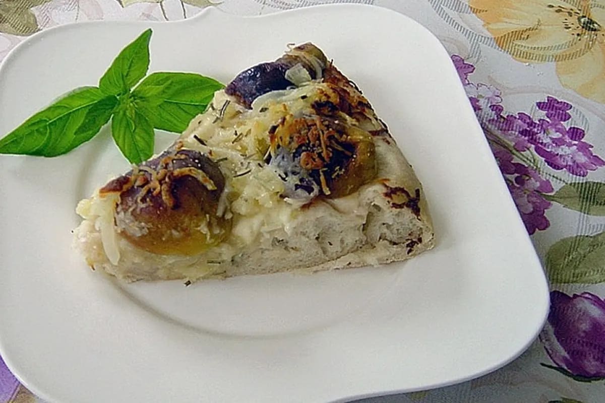 Frisch gebackene Pizza mit halbierten Feigen, zerbröckeltem Ziegenkäse, goldbraunen Zwiebelringen, Mozzarella und Rosmarin auf knuspriger Kruste